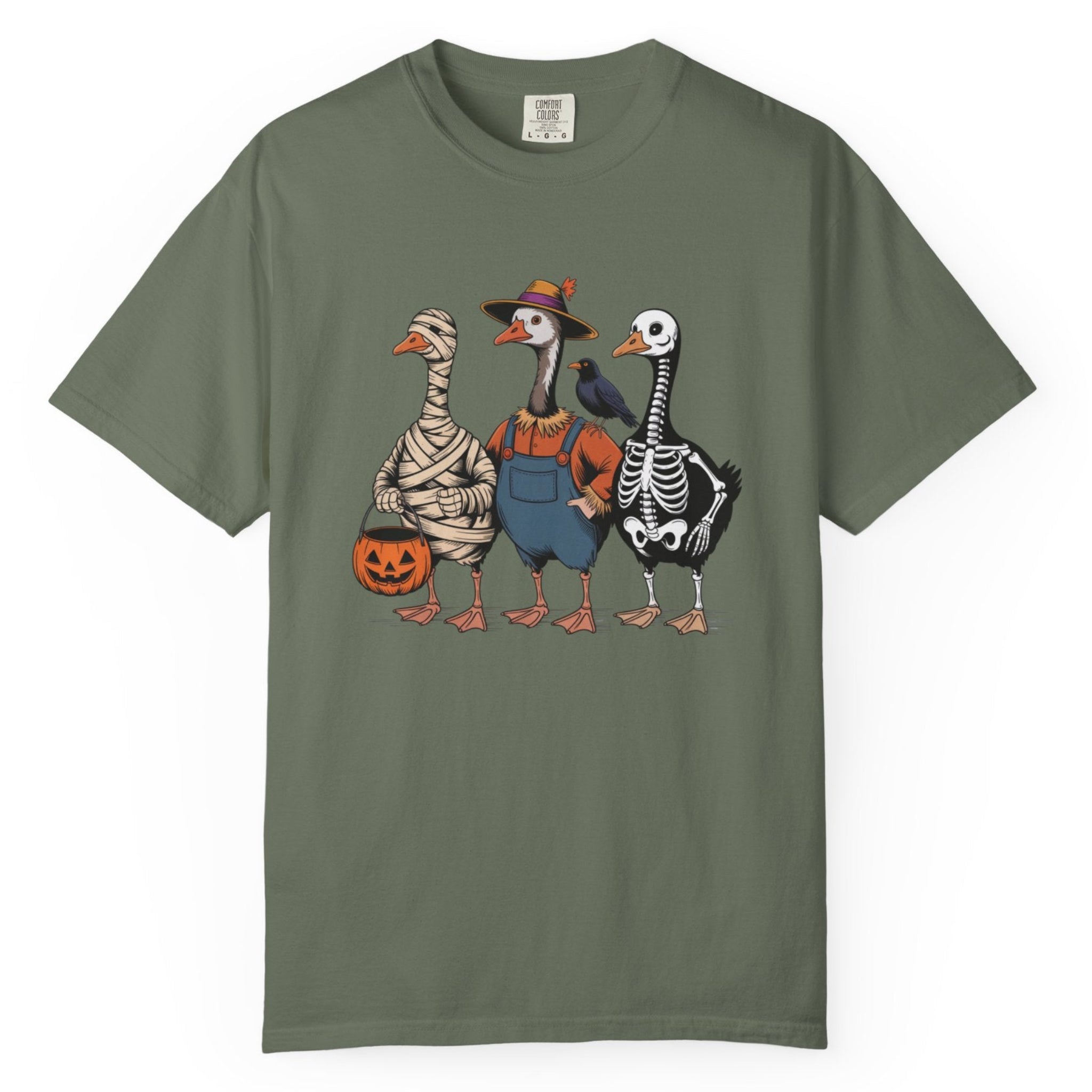 An light green short-sleeve t-shirt with a graphic print of three geesedressed in Halloween costumes (mummy, turkey, and skeleton) on the front, displayed against a plain white background.