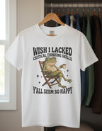 A white short-sleeve crewneck t-shirt featuring a graphic of a green frog sitting in a wooden director's chair and holding a coffee mug, with humorous text above and below the illustration.