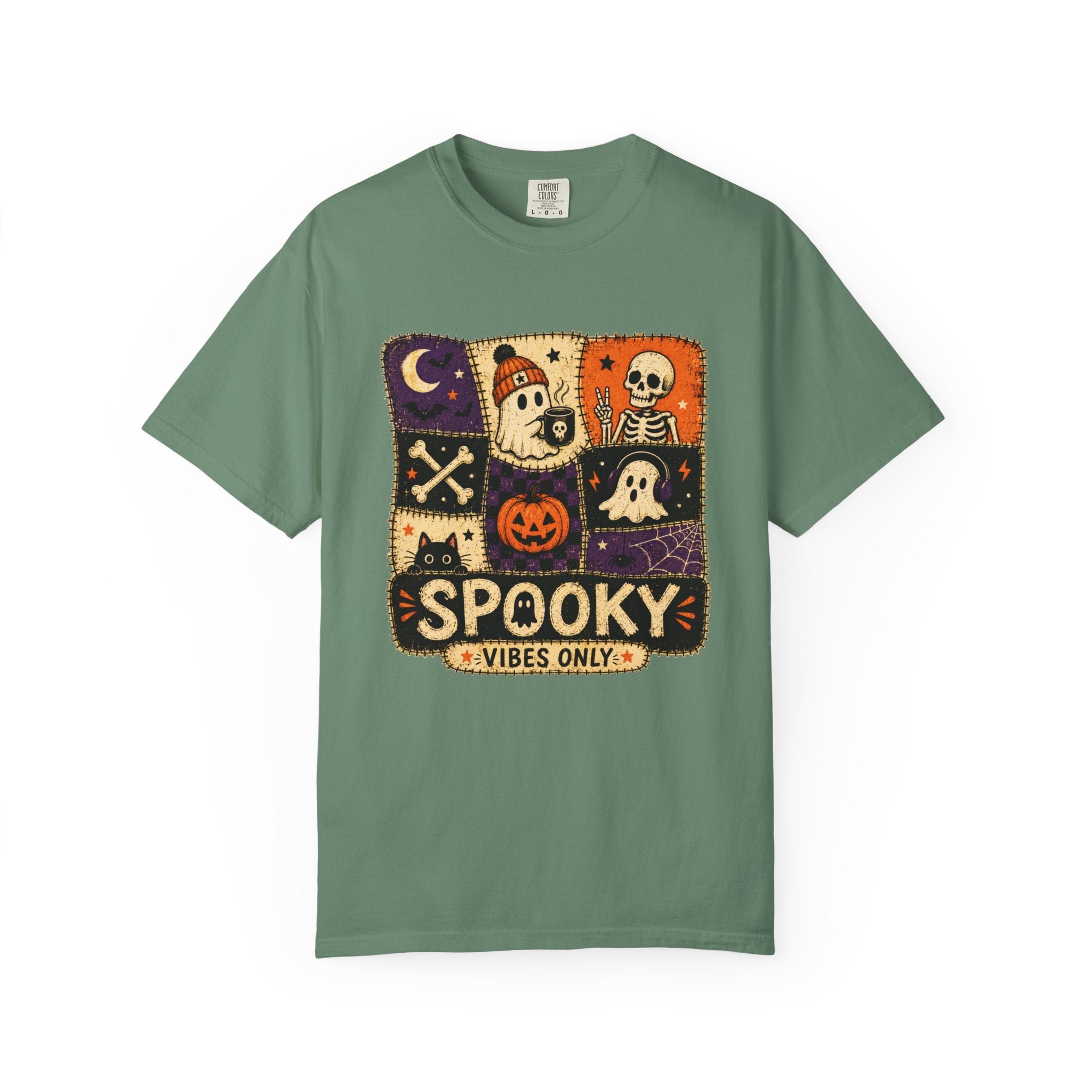 A sage green short-sleeve t-shirt with a central square graphic featuring Halloween-themed illustrations like a skeleton, ghost, pumpkin, and moon, with the text 'SPOOKY VIBES ONLY'.