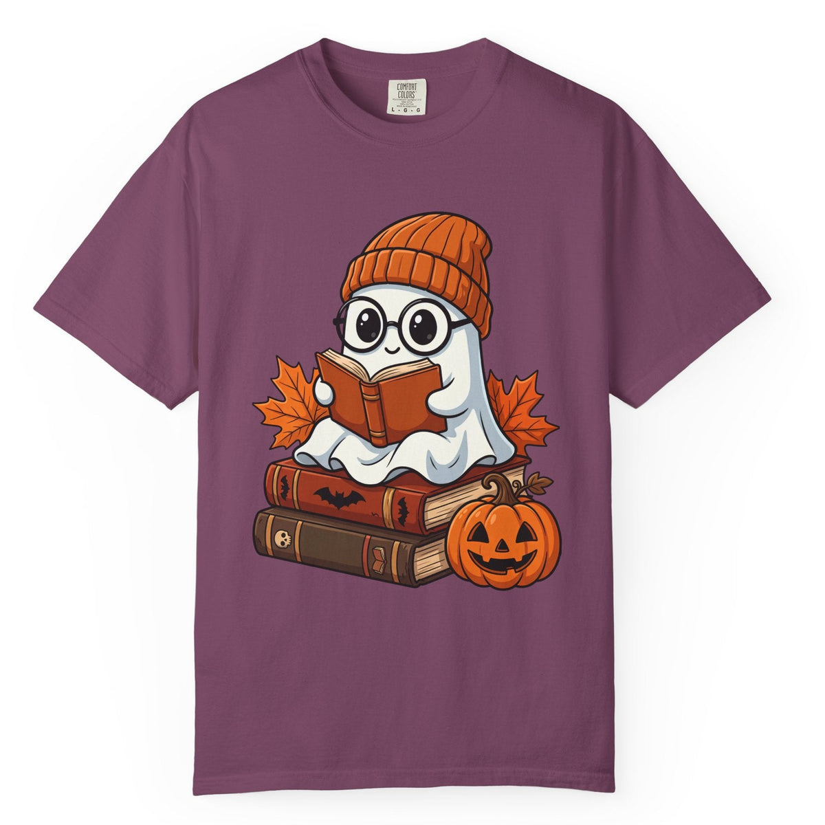A purple short-sleeve crewneck t-shirt featuring a cartoon graphic of a cute ghost wearing glasses and an orange knit beanie, sitting on a stack of books and reading an orange book next to a jack-o'-lantern pumpkin and autumn leaves.