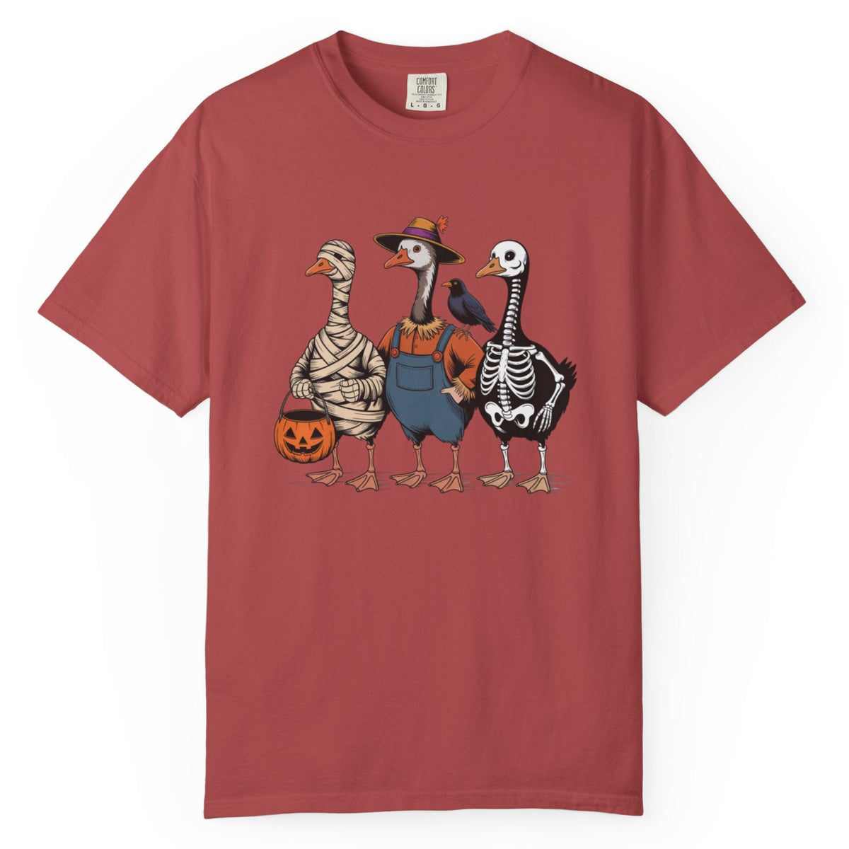 A crimson short-sleeve crewneck t-shirt featuring a graphic print of three geese in Halloween costumes (mummy, cowboy, and skeleton) standing next to a jack-o'-lantern pumpkin.