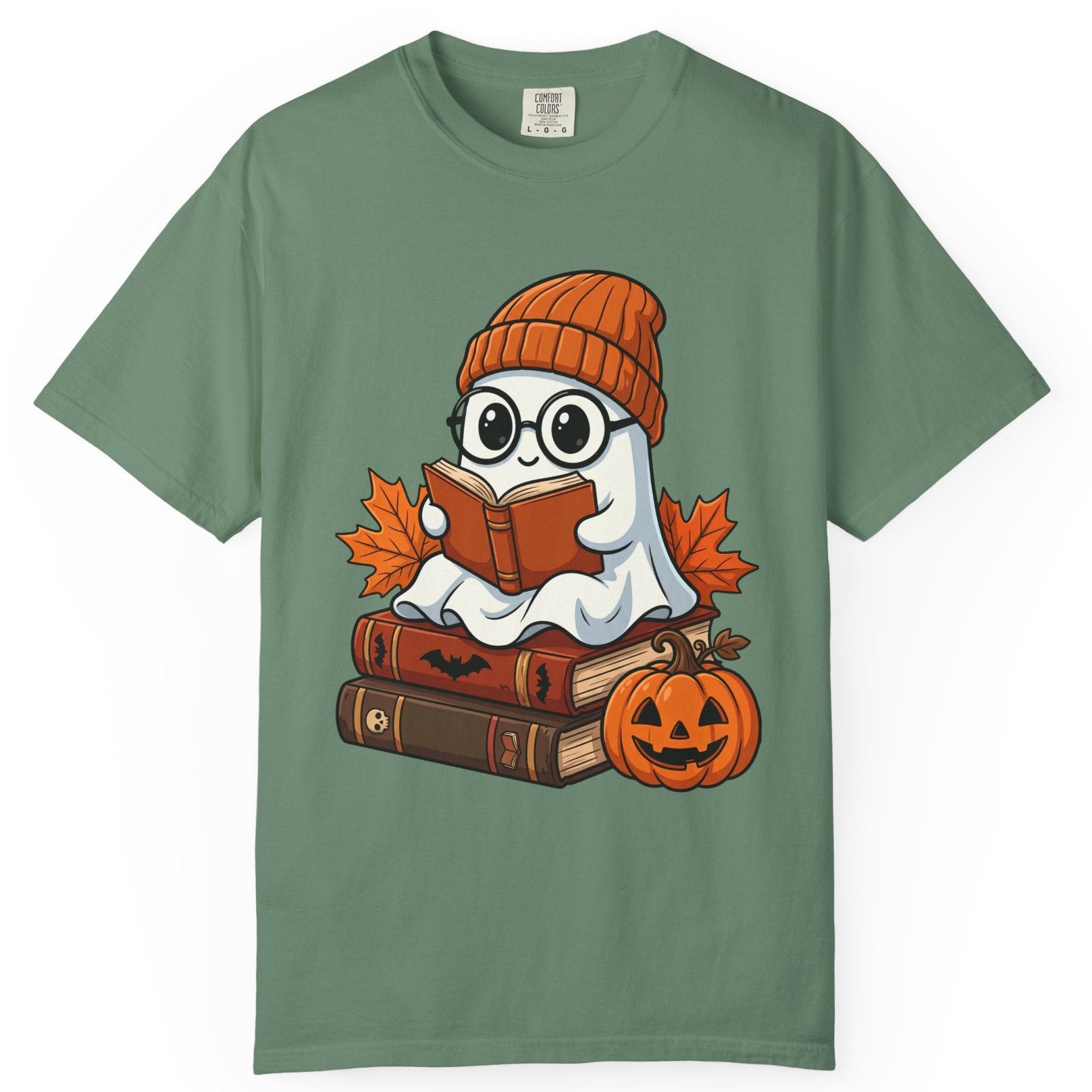 A light green short-sleeve t-shirt with a cartoon graphic of a ghost wearing an orange beanie and reading a book, surrounded by autumn leaves, books, and a jack-o'-lantern pumpkin.