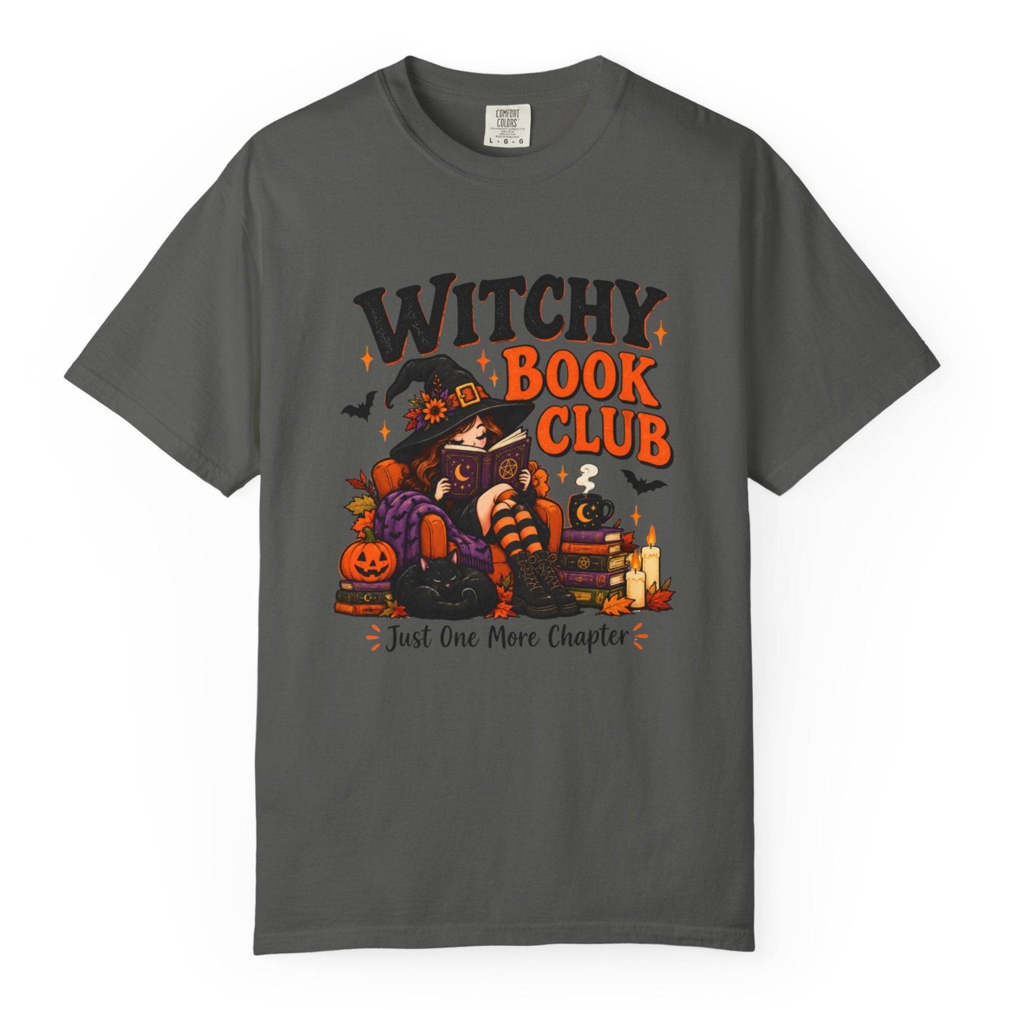 A dark gray crewneck t-shirt featuring a colorful graphic of a witch sitting on a pumpkin next to a stack of books, with the text 'WITCHY BOOK CLUB' and 'Just One More Chapter'.