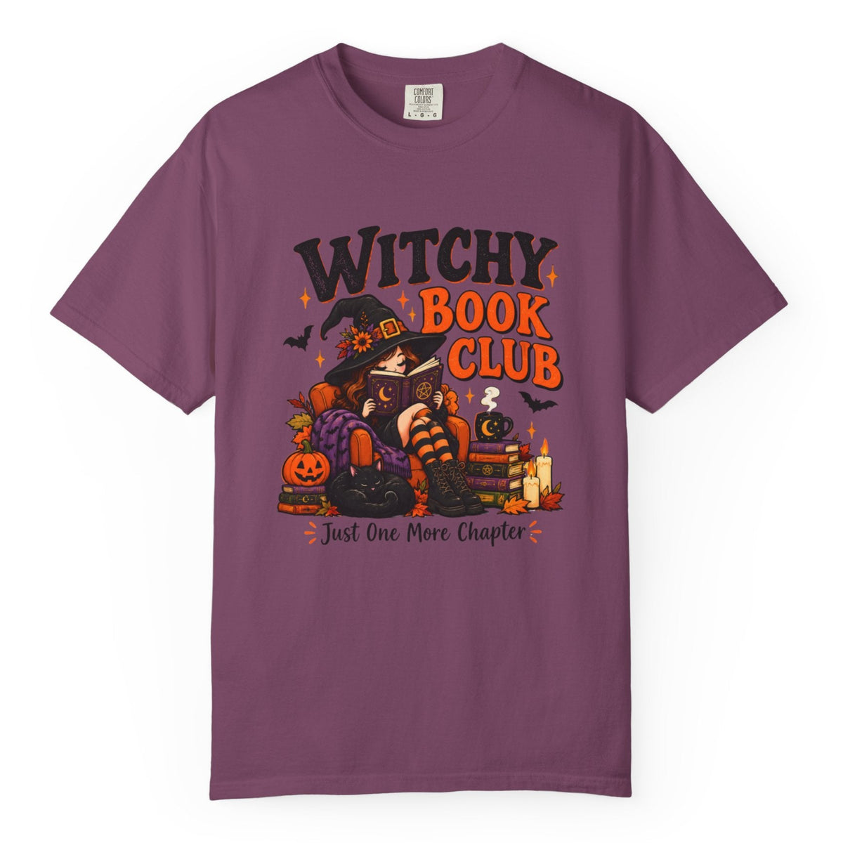 A purple short-sleeve crewneck t-shirt featuring a colorful graphic on the front with the text 'WITCHY BOOK CLUB' and 'Just One More Chapter' surrounding an illustration of a witch, pumpkin, and candles.