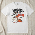 A white short-sleeve crewneck t-shirt featuring a Halloween graphic of a goose dressed as a witch holding a jack-o'-lantern next to pumpkins, with the text 'HONK OR TREAT' and small bats.
