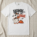 A white short-sleeve crewneck t-shirt featuring a Halloween graphic of a goose dressed as a witch holding a jack-o'-lantern next to pumpkins, with the text 'HONK OR TREAT' and small bats.