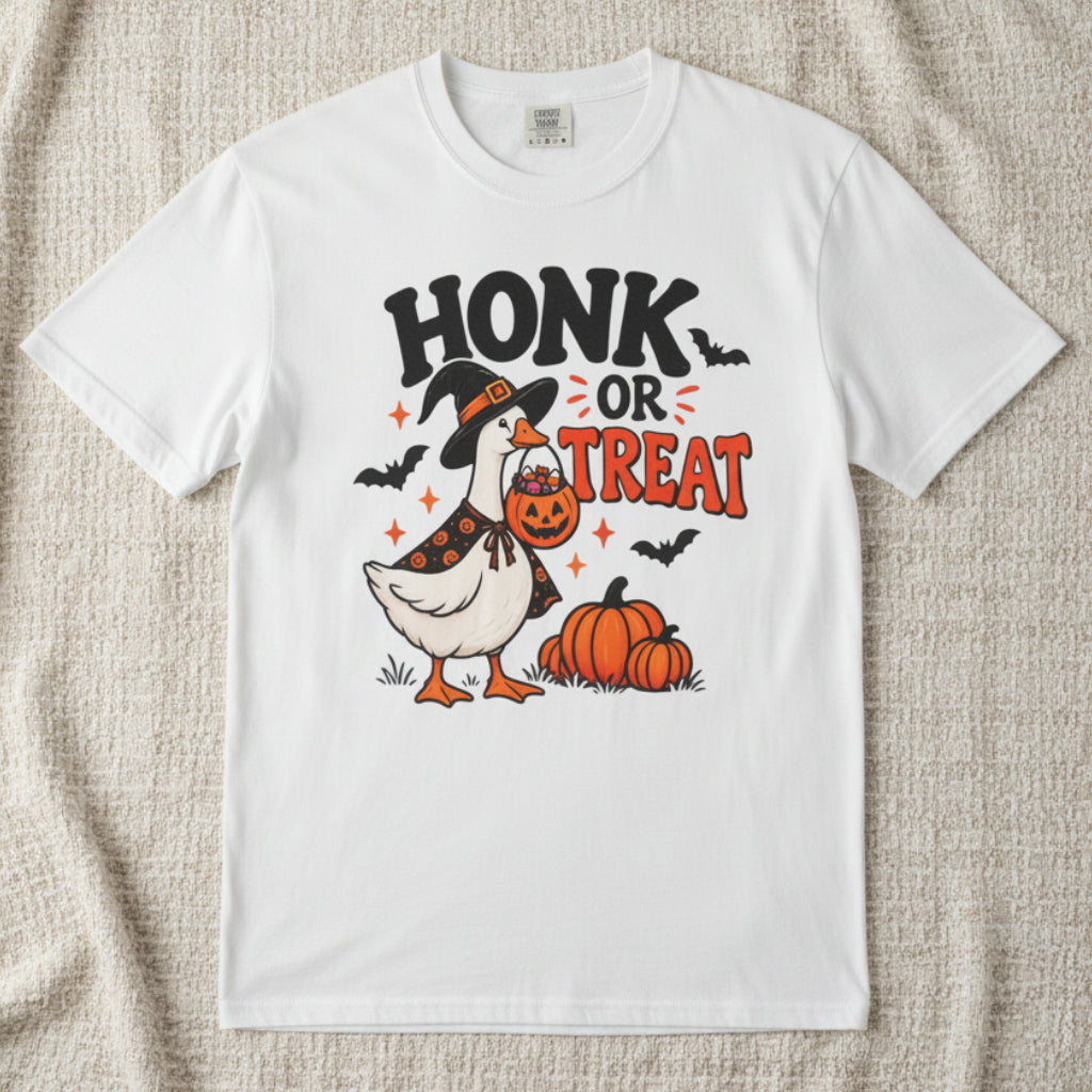 A white short-sleeve crewneck t-shirt featuring a Halloween graphic of a goose dressed as a witch holding a jack-o'-lantern next to pumpkins, with the text 'HONK OR TREAT' and small bats.
