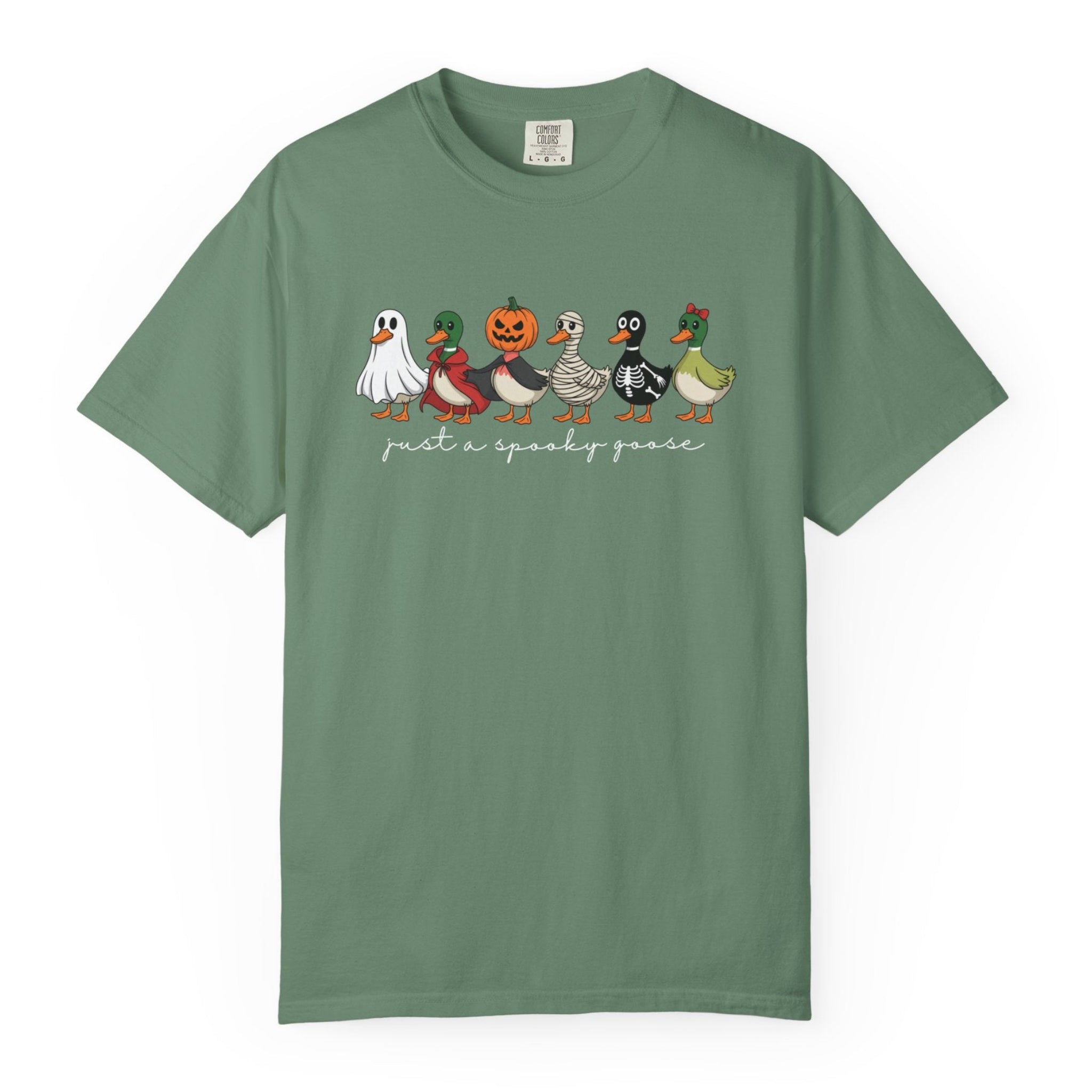 A light green short-sleeve t-shirt with a graphic of six cartoon ducks dressed in Halloween costumes walking in a line, with the text 'just a spooky goose' printed below them.