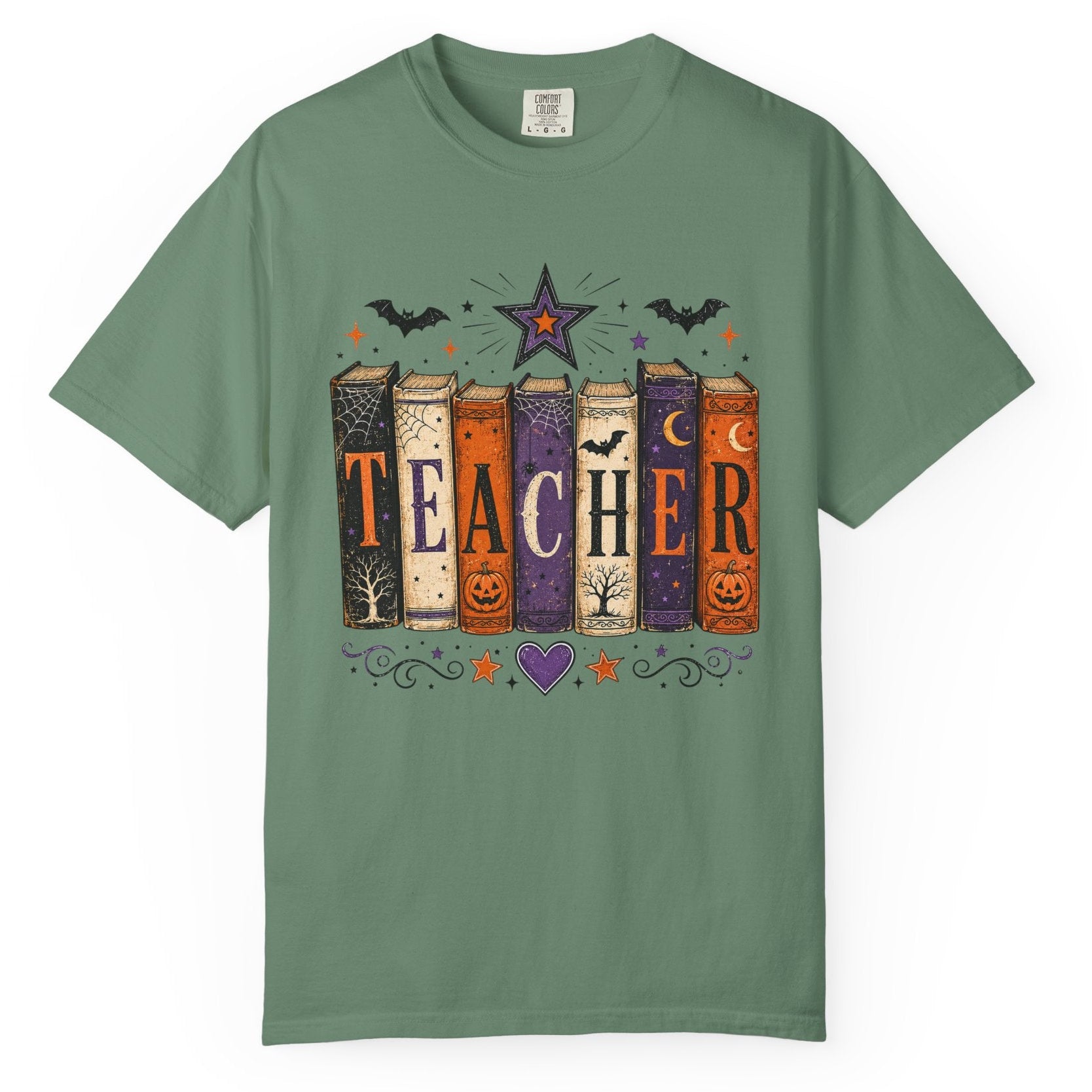 A sage green short-sleeve t-shirt with a Halloween-themed graphic on the chest. The graphic features the word 'TEACHER' spelled out vertically using six colorful book spines decorated with autumn motifs like pumpkins, bats, and stars.