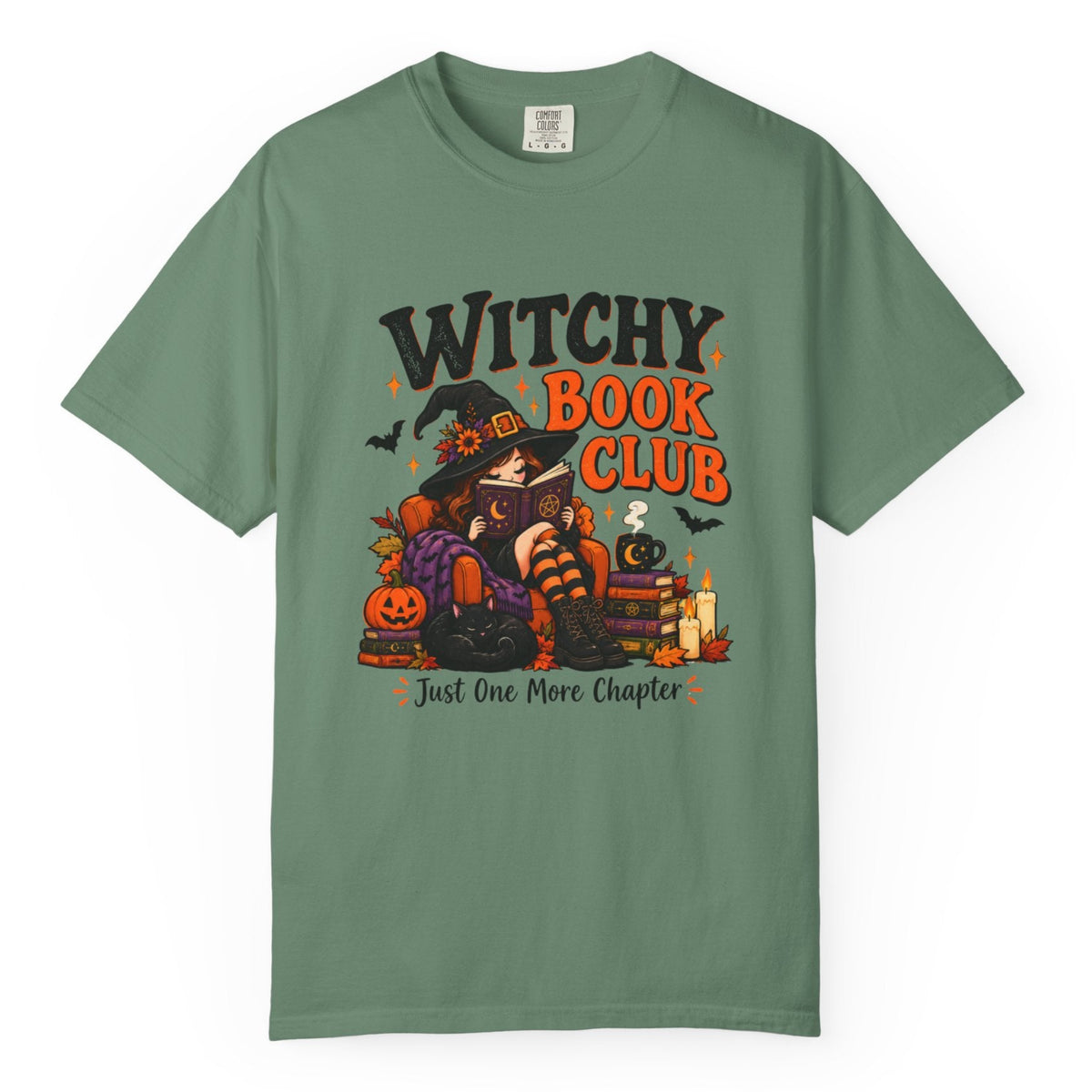 A sage green short-sleeve t-shirt with a colorful graphic on the front that reads 'WITCHY BOOK CLUB' and 'Just One More Chapter' above an illustration of a witch, pumpkin, and candles.