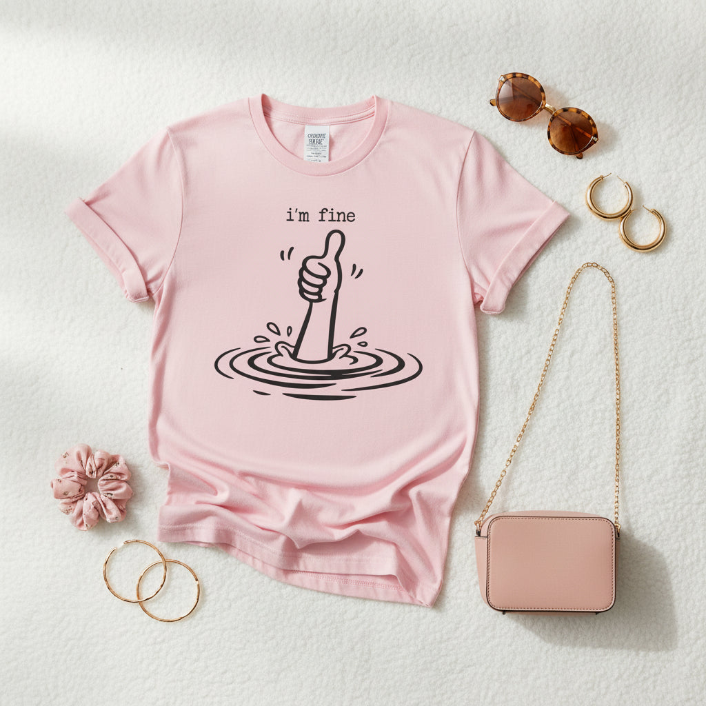 A light pink short-sleeve crewneck t-shirt featuring a black graphic of a hand giving a thumbs-up with the text 'i'm fine' above it, displayed on a clean white background.