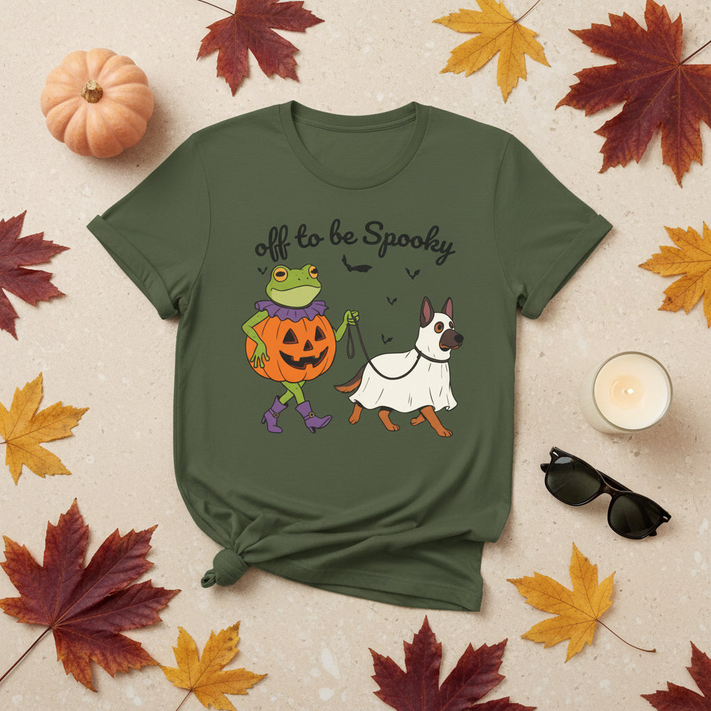 An olive green short-sleeve crewneck t-shirt featuring a Halloween graphic of a green frog in a pumpkin costume and a white dog in a ghost costume, with the text 'off to be Spooky' above them.