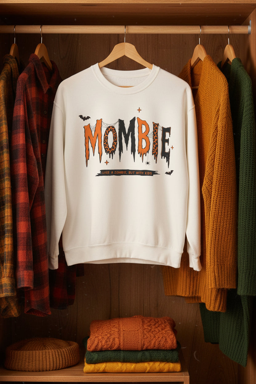 An off-white crewneck sweatshirt featuring a Halloween-themed graphic on the chest that reads 'MOMBIE' in dripping orange and black letters with leopard print details