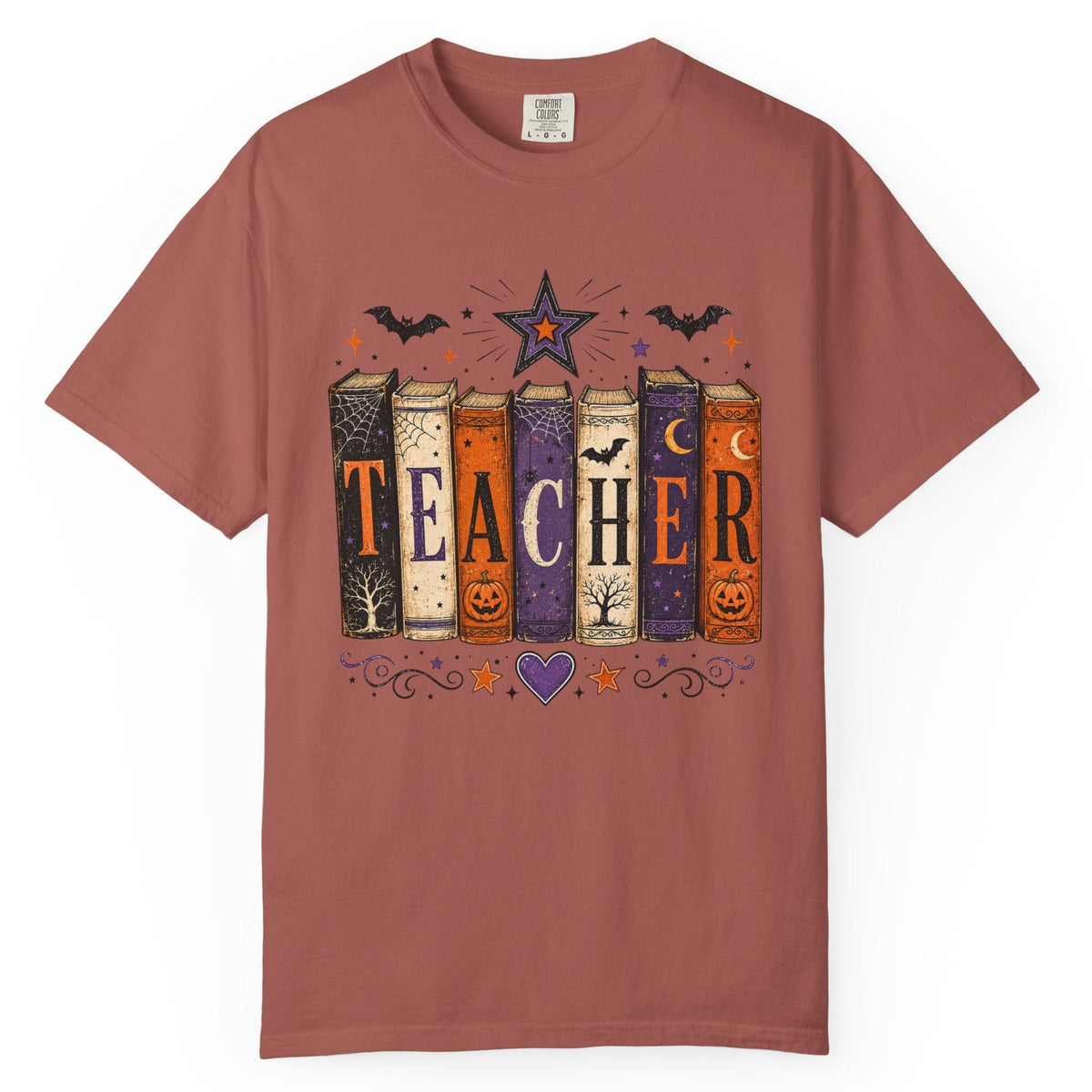 A dusty rose short-sleeve crewneck t-shirt featuring a Halloween-themed graphic of books spelling 'TEACHER' with bats, a star, and pumpkins on a white background.