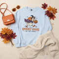 A light blue crewneck sweatshirt featuring a cartoon graphic of a goose dressed as a witch holding a jack-o'-lantern, with the text 'SPOOKY GOOSE ON THE LOOSE' printed below.