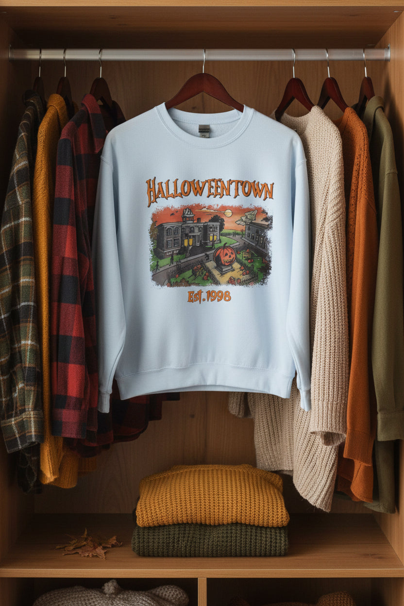 A light blue crewneck sweatshirt featuring a Halloween-themed graphic print on the front with the text 'HALLOWEENTOWN' and 'Est. 1998' surrounding an illustration of haunted houses and a jack-o'-lantern.