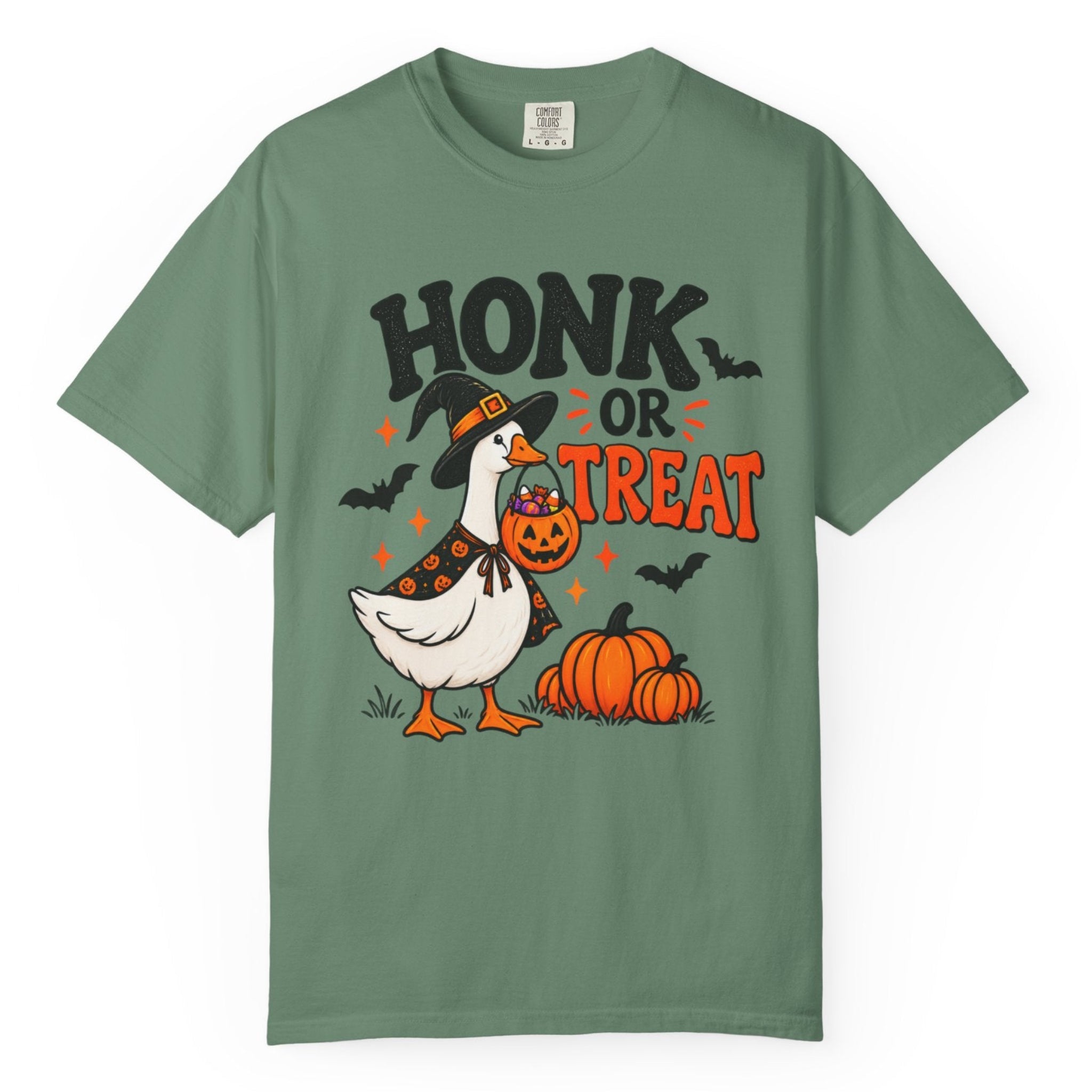 Alight green short-sleeve crewneck t-shirt featuring a Halloween graphic of a goose dressed as a witch holding a jack-o'-lantern next to pumpkins, with the text 'HONK OR TREAT'.