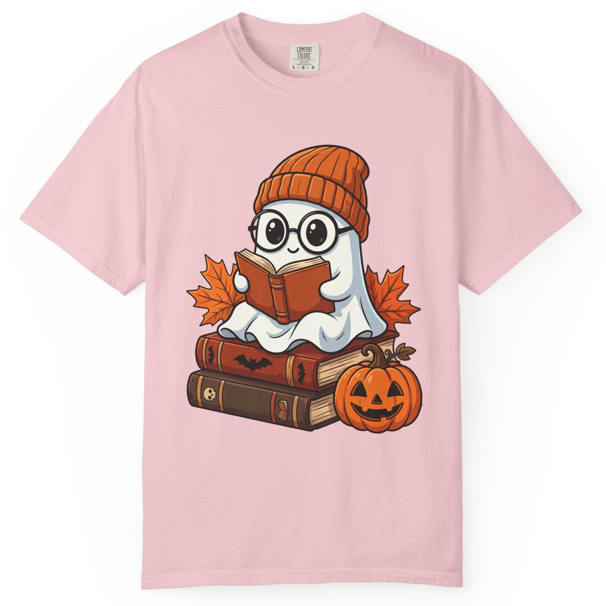 A light pink short-sleeve crewneck t-shirt featuring a cartoon graphic of a ghost wearing a knit orange beanie and reading a book, surrounded by autumn leaves, old books, and a jack-o'-lantern pumpkin.