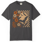 A dark gray short-sleeve t-shirt with a vintage-style graphic print on the front. The print features a silhouette of a person riding a horse, surrounded by orange and cream daisies, and framed by a beige and dark gray checkerboard pattern.