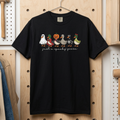 A black short-sleeve graphic t-shirt hanging on a wooden pegboard in a workshop setting. The graphic shows a row of cartoon spooktacular ducks in Halloween costumes with the text 'just a spooky goose' underneath.