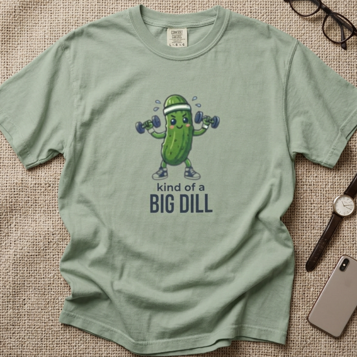 A sage green graphic t-shirt. The t-shirt features a cartoon pickle character lifting dumbbells with the text 'kind of a BIG DILL' printed below.
