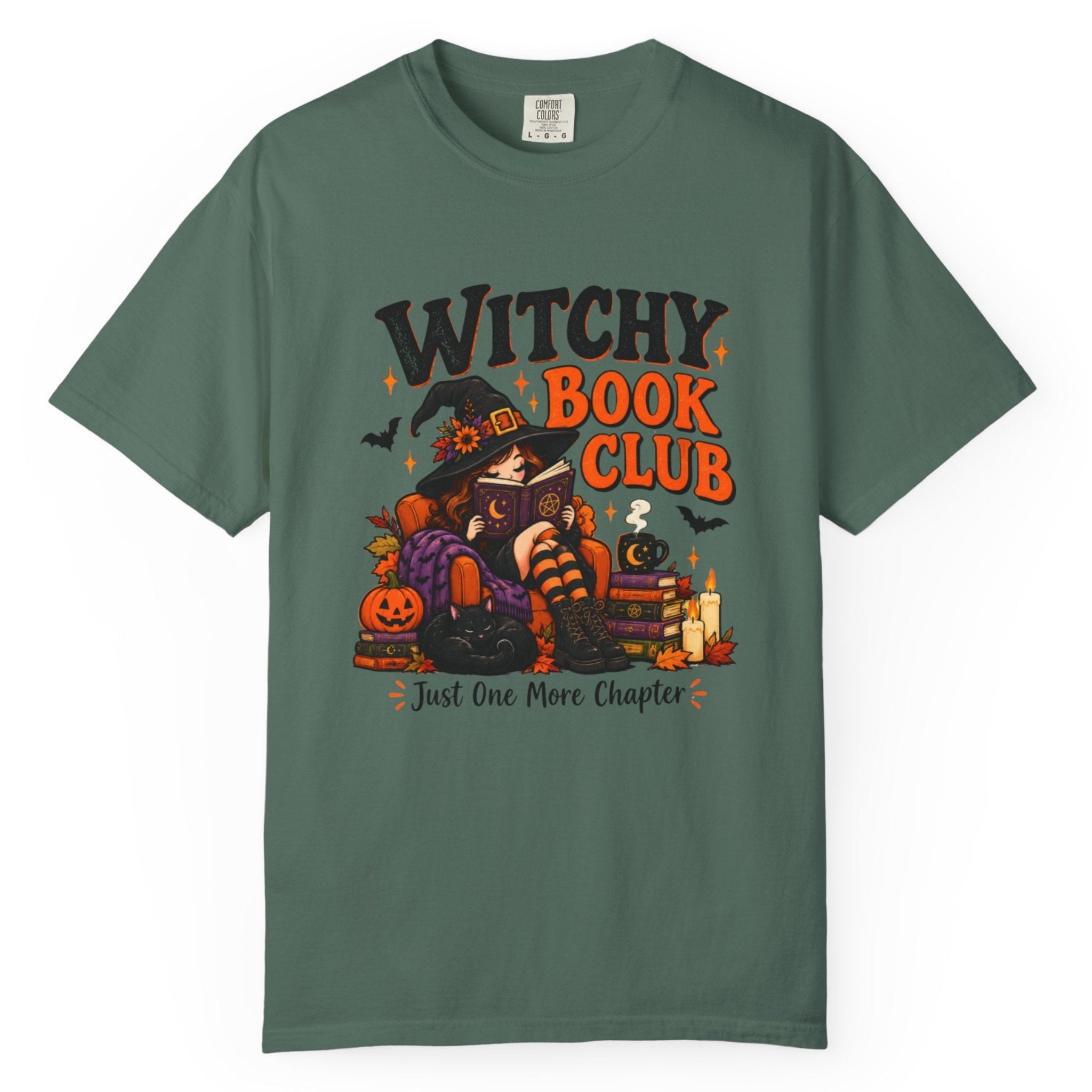 A dark green short-sleeve t-shirt with a colorful graphic on the front that reads 'Witchy Book Club' and 'Just One More Chapter', featuring an illustration of a witch, a pumpkin, a candle, and a book.