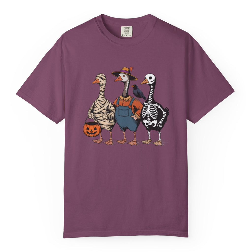 A purple short-sleeve crewneck t-shirt featuring a graphic print of three geese dressed in Halloween costumes (as mummy, skeleton, and in blue overalls), set against a plain white background.