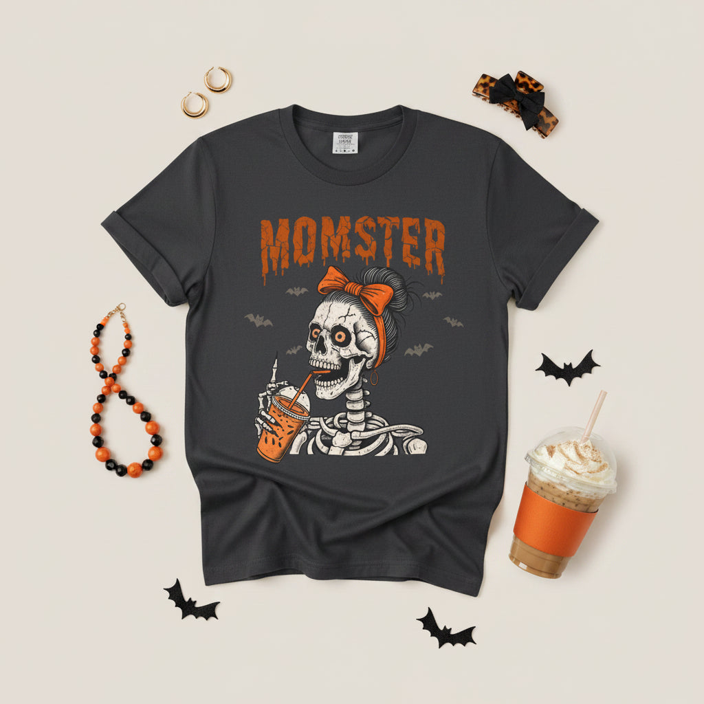 A dark gray crewneck t-shirt featuring a Halloween graphic of a skeleton wearing an orange bow and holding an orange drink, with the word 'MOMSTER' printed above in orange.
