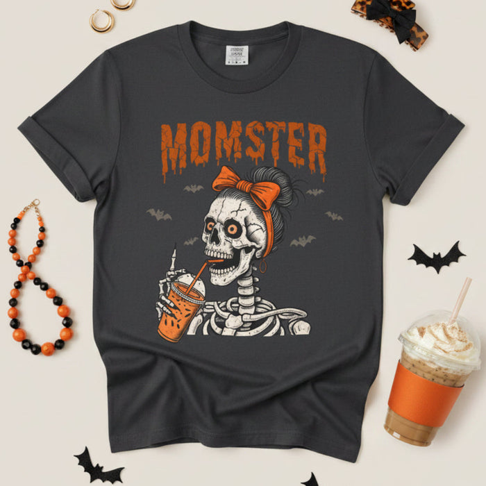 A dark gray crewneck t-shirt featuring a Halloween graphic of a skeleton wearing an orange bow and holding an orange drink, with the word 'MOMSTER' printed above in orange.