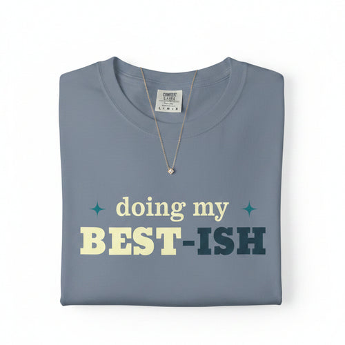 A slate blue crewneck t-shirt with a graphic text print reading 'doing my BEST-ISH' in cream and dark teal lettering, displayed on a clean white background.
