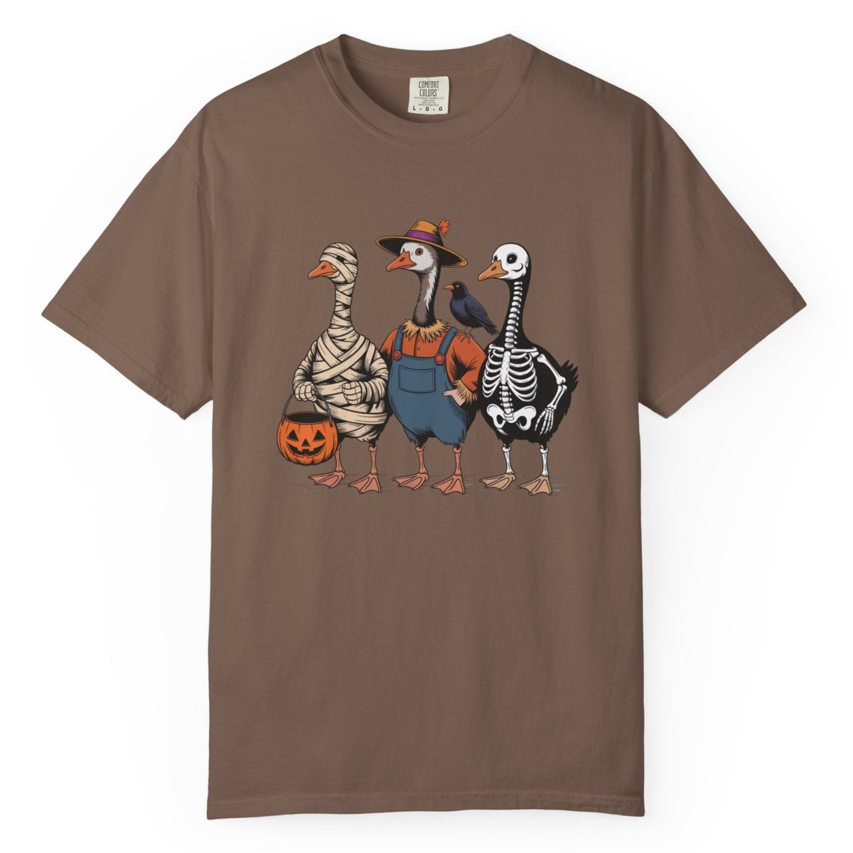 A brown short-sleeve crewneck t-shirt featuring a graphic print of three geese dressed in Halloween costumes (mummy, skeleton, and cowboy), holding pumpkin buckets, against a plain white background.