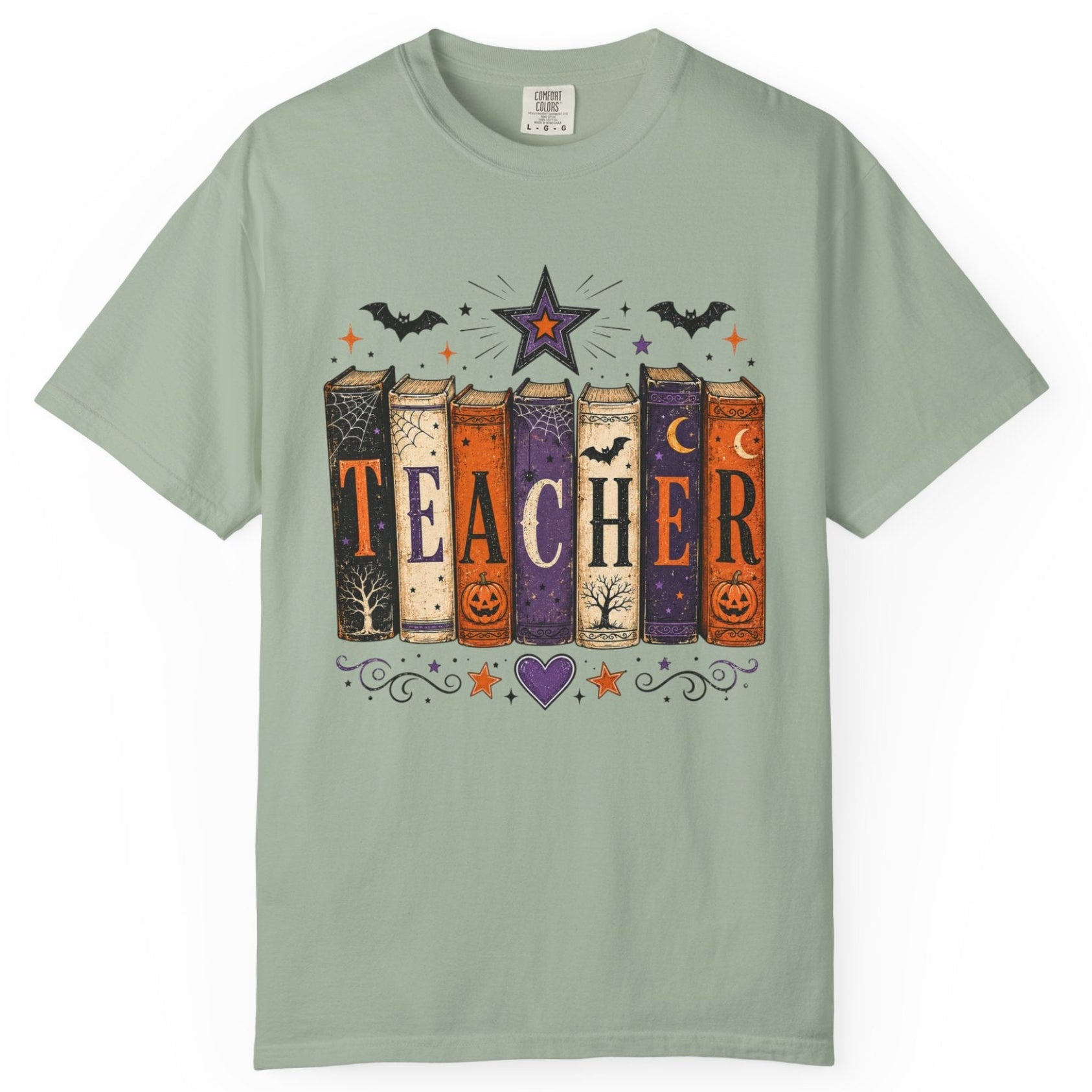 A sage green short-sleeve t-shirt with a Halloween-themed graphic on the chest depicting colorful books spelling 'TEACHER' with bats, a star, and pumpkins.