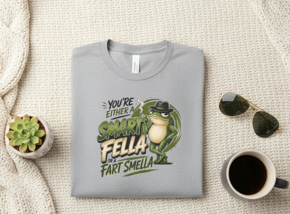 A sport gray short-sleeve crewneck t-shirt featuring a graphic print of a frog wearing a hat and sunglasses next to the text 'YOU'RE EITHER A SMART FELLA OR FART SMELLA'.