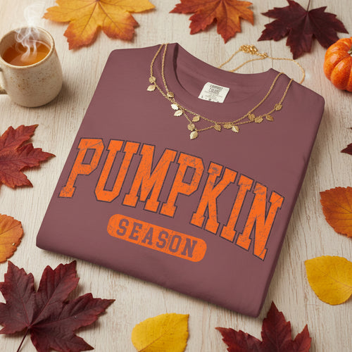 A folded brick color crewneck t-shirt with 'PUMPKIN SEASON' printed in orange varsity-style lettering on the front