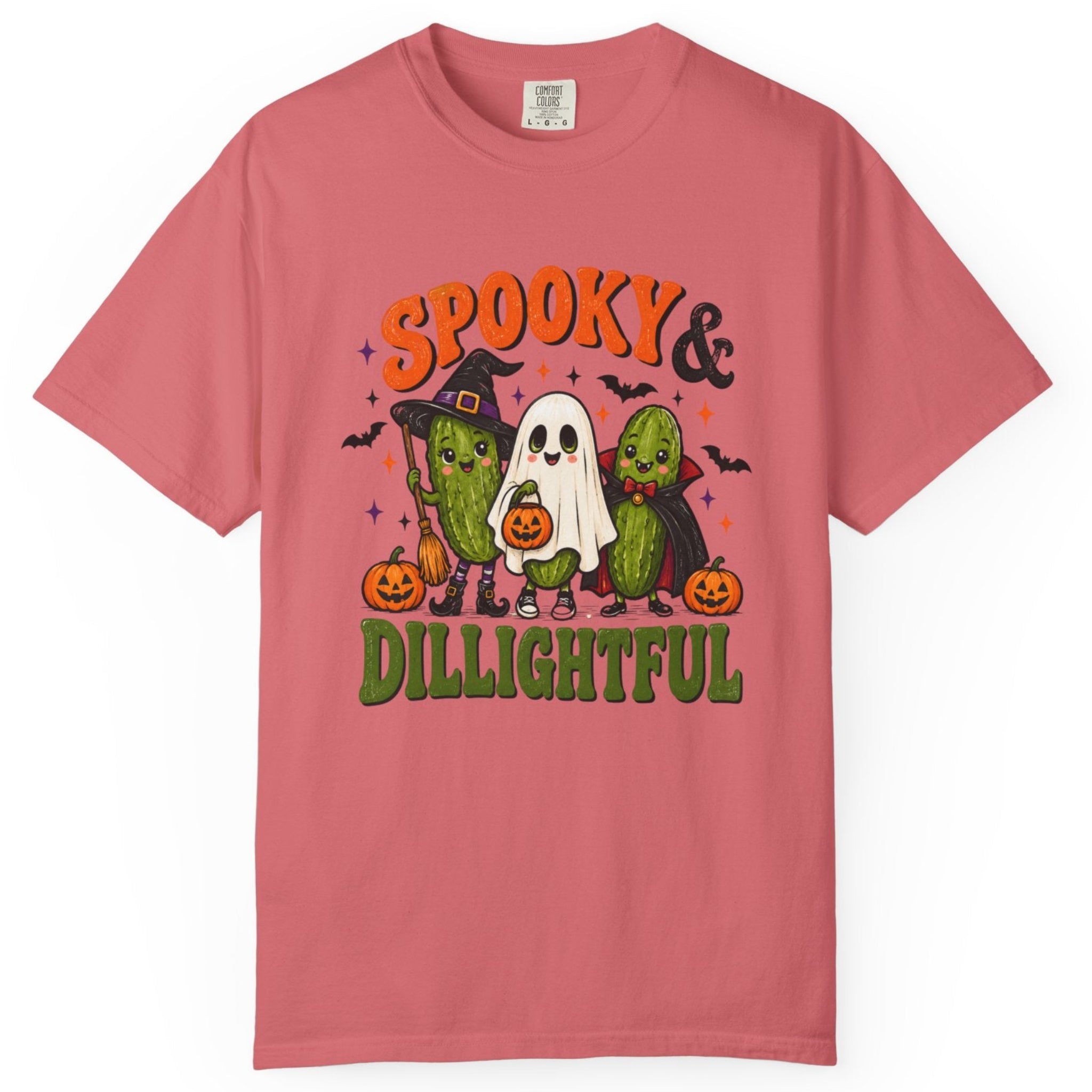A pink short-sleeve crewneck t-shirt featuring a colorful graphic of three cute cactus characters dressed in Halloween costumes (witch, ghost, and zombie) with pumpkins, under the text 'SPOOKY & DILIGHTFUL'.