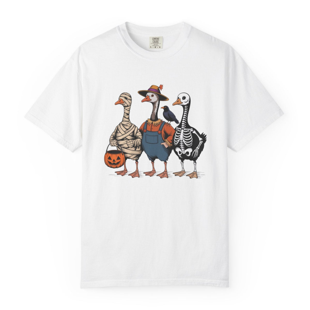 A white short-sleeve crewneck t-shirt featuring a graphic print of three cartoon Halloween geese dressed as a mummy, a skeleton, and a cowboy, standing together and holding a jack-o'-lantern.