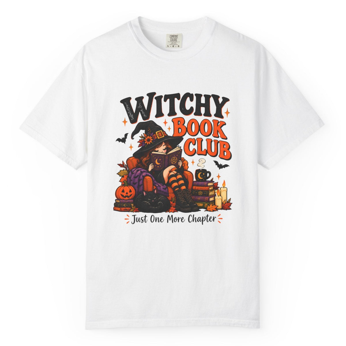 A white short-sleeve crewneck t-shirt featuring a colorful graphic print on the front with the text 'WITCHY BOOK CLUB' and 'Just One More Chapter' surrounding an illustration of a witch, a pumpkin, a cat, and candles.
