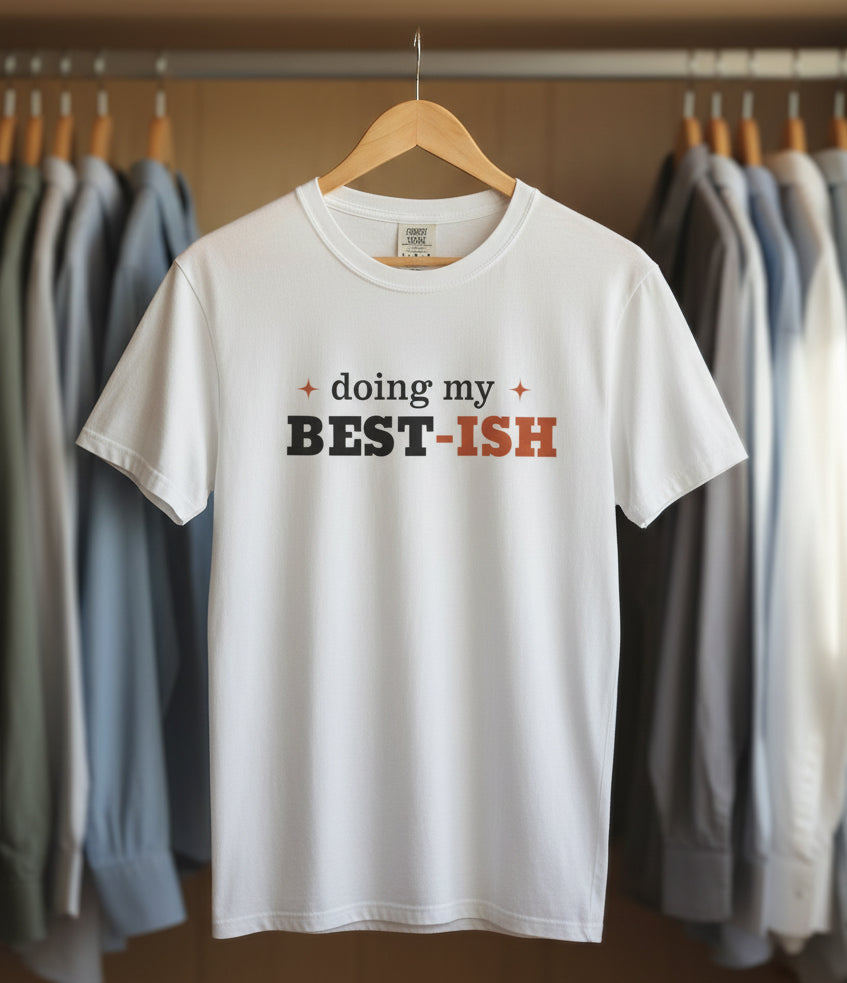 A white short-sleeve crewneck t-shirt with a graphic text print reading 'doing my BEST-ISH' across the chest. The words 'doing my' and 'BEST-ISH' are styled in black and orange, respectively, with small orange starburst accents on either side.