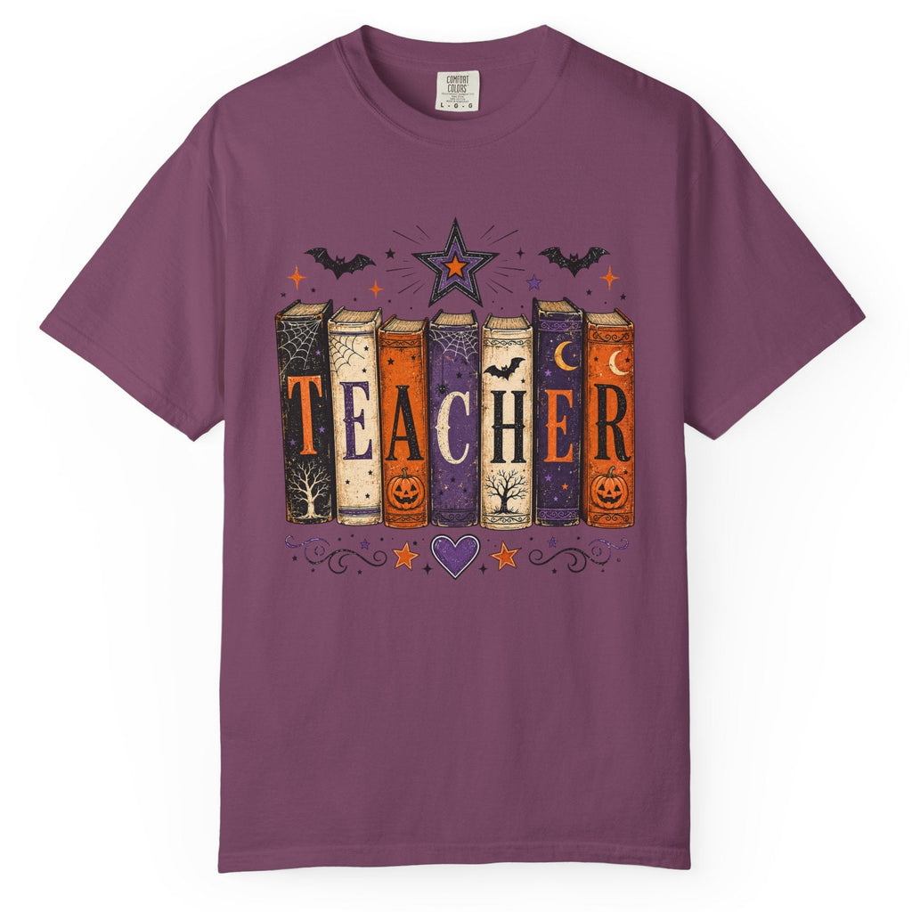 A purple short-sleeve crewneck t-shirt featuring a Halloween-themed graphic of colorful books spelling 'TEACHER' with bats, stars, and pumpkins.