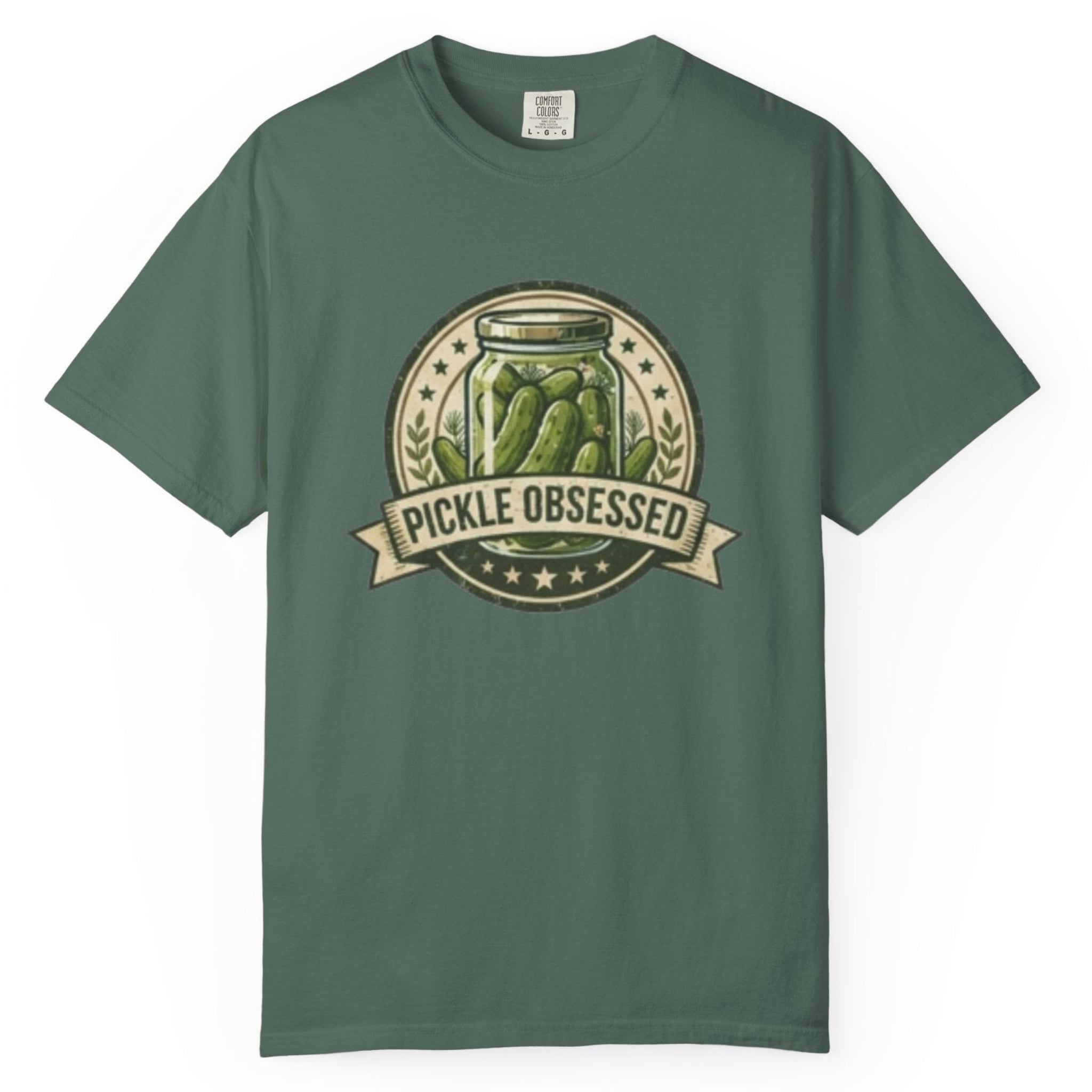 A  blue short-sleeve t-shirt hanging on a wooden hanger against a light wood pegboard wall. The shirt features a circular graphic print with a jar of pickled green onions and the words 'PICKLE OBSESSED' in a banner.