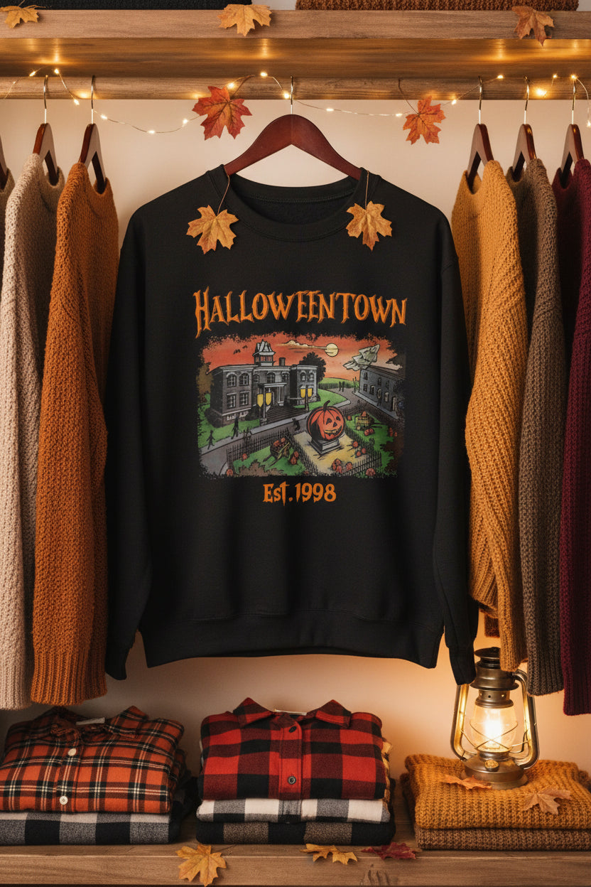 A black crewneck sweatshirt featuring a colorful graphic print of a haunted Halloween town with the text 'HALLOWEENTOWN' and 'Est. 1998'.
