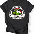 Black Official Christmas Diller graphic T-shirt design featuring a green pickle Santa wearing sunglasses and holding a Christmas present, with festive trees and bold holiday lettering.