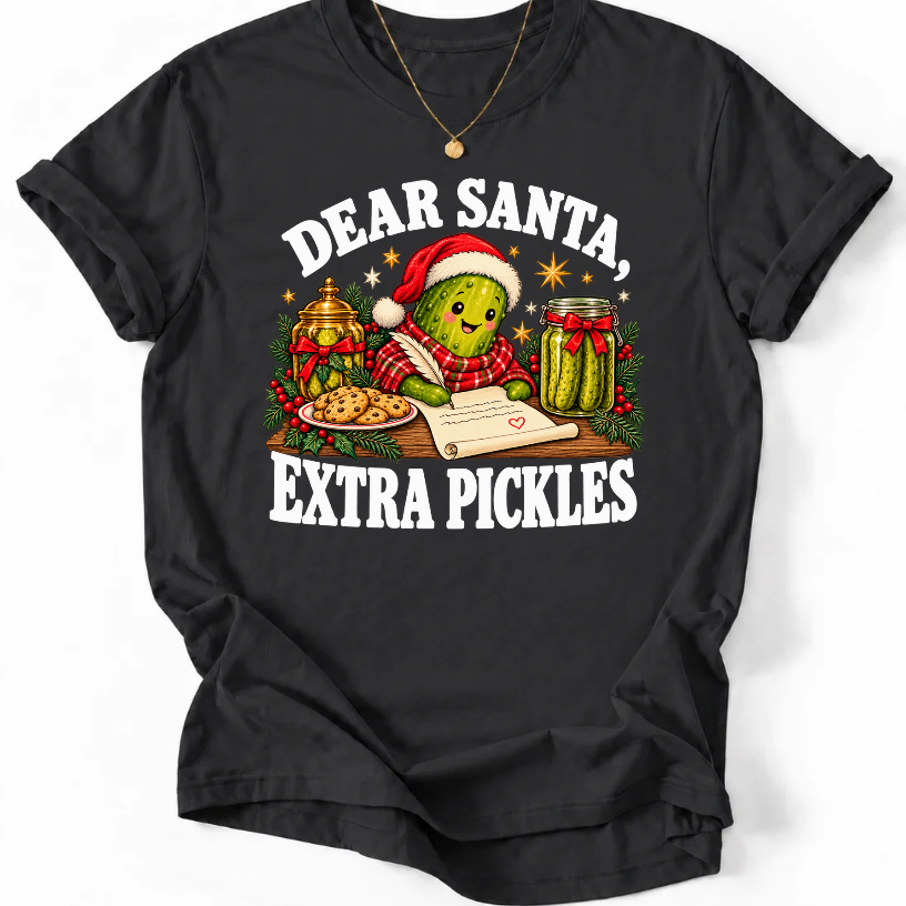Black ‘Dear Santa, Extra Pickles’ T-shirt featuring a Santa-hat pickle writing a letter beside cookies and pickles.”
