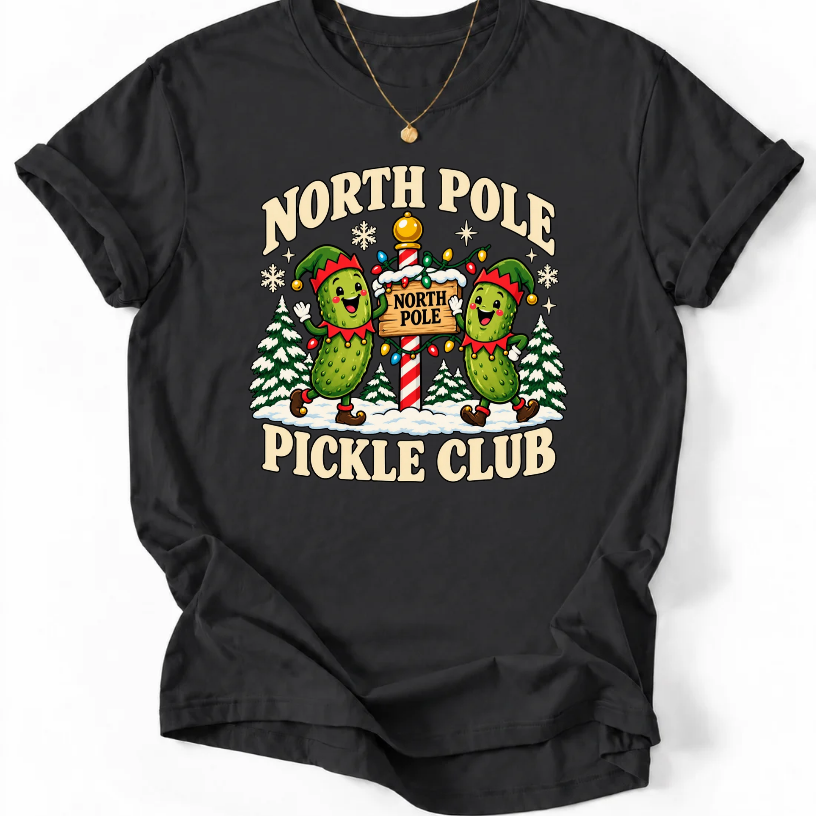 Black T-shirt with “North Pole Pickle Club” lettering and two pickle elves beside a candy cane signpost and snowy trees.