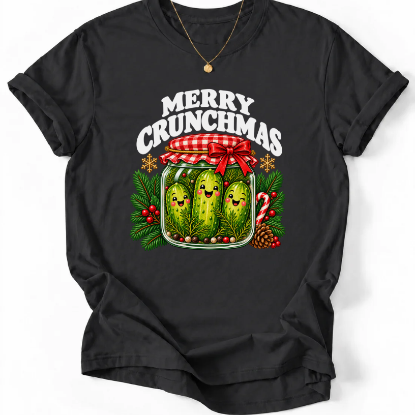 Black T-shirt with “Merry Crunchmas” lettering above three smiling pickles in a jar decorated with a red bow and Christmas greenery.
