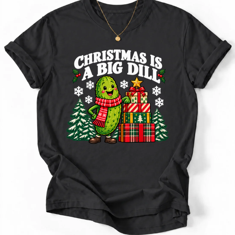 Black T-shirt with “Christmas Is a Big Dill” lettering and a smiling pickle in a red scarf beside stacked gifts and snowy trees.