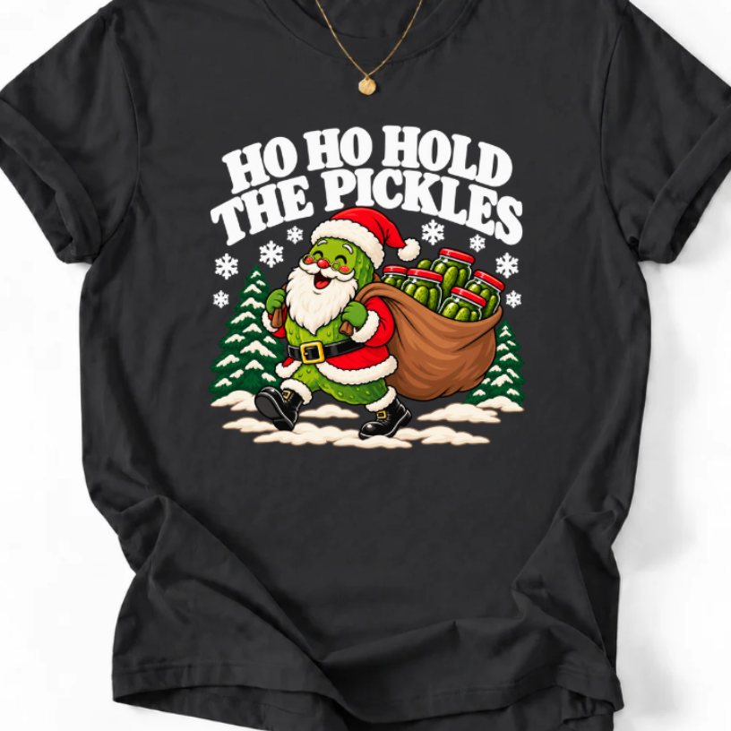 Black T-shirt with “Ho Ho Hold the Pickles” lettering and a pickle dressed as Santa carrying a sack of pickle jars beside snowy trees.