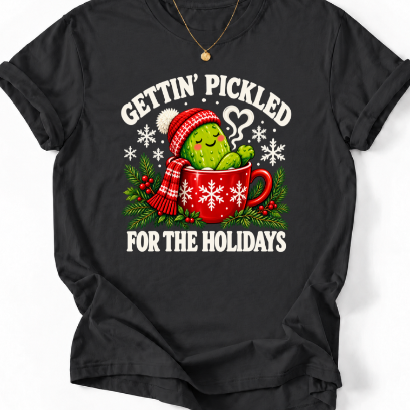 Black Gettin’ Pickled for the Holidays T-shirt featuring a pickle in a red snowflake mug, wearing a knit hat and scarf.”
