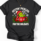 Black Gettin’ Pickled for the Holidays T-shirt featuring a pickle in a red snowflake mug, wearing a knit hat and scarf.”