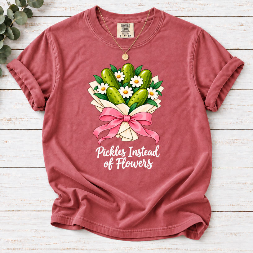 Crimson T-shirt with a pickle and daisy bouquet, pink bow, and white ‘Pickles Instead of Flowers’ lettering